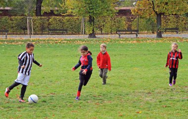 children are playing football in city park clipart