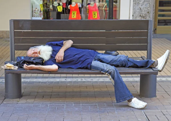 Oude man is slapen op een bankje buiten in Sofia, Bulgarije — Stockfoto
