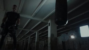 Erkek atlet boxer kum torbası karanlık bir stüdyoda dramatik sinirli aydınlatma ile