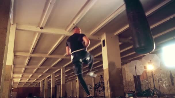 Erkek atlet boxer kum torbası karanlık bir stüdyoda dramatik sinirli aydınlatma ile — Stok video