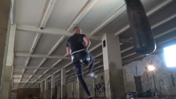 Erkek atlet boxer kum torbası karanlık bir stüdyoda dramatik sinirli aydınlatma ile — Stok video