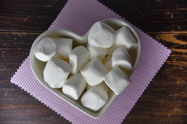 Morbido marshmallow bianco in ciotola sagomata a cuore su vecchio tavolo in legno con spazio copia da vicino . — Foto Stock