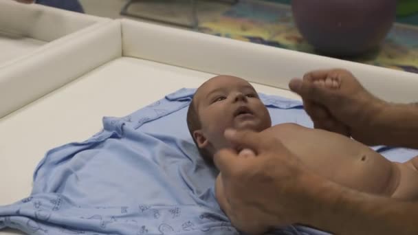 赤ん坊は脚と腕のマッサージをするテーブルの上に横たわっていた 小さな赤ちゃんの指健康的なライフスタイル陸上競技テーブルの上に寝そべっている少年 — ストック動画