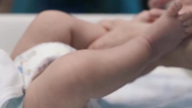 Bebek masanın üzerinde uzanıp kollarına ve bacaklarına masaj yapıyor. Küçük bebek parmakları. Sağlıklı bir yaşam tarzı. Atletizm. Masada yatan çocuk.