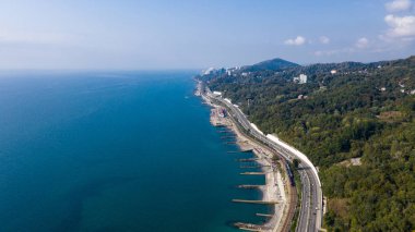 Hava fotoğrafçılığı. Deniz kıyısındaki yol. Rus tatil beldesi Sochi. Yeşil ağaçlar. Mavi deniz. Plaj şeridi. Deniz kıyısı boyunca demiryolu. Kuş bakışı.