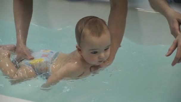 Egy kisfiú a medencében. Úszni tanulok. Csecsemő. Anyák kezei. Víz. Egészségére. Sport. Gyógyszer. — Stock videók