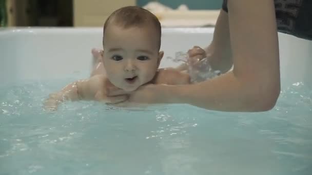 En liten pojke i poolen. Att lära sig simma. Bröstbebis. Mödrar händer. Vatten. Hälsa. Idrott. Medicin. — Stockvideo