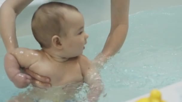 En liten pojke i poolen. Att lära sig simma. Bröstbebis. Mödrar händer. Vatten. Hälsa. Idrott. Medicin. — Stockvideo