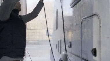 Avrupa uyruklu genç bir adam araba yıkamada araba yıkıyor. Mevsimlik karavan, motorlu taşıt temizleme, basınç makinası. Karavan kampçısı. Beyaz Erkekler