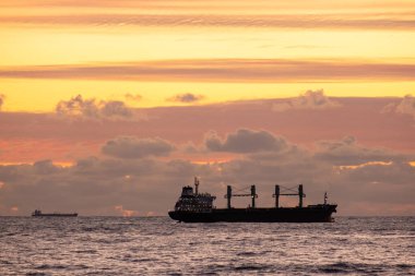 Denizin üzerinde gün batımı. Ufukta bir donanma gemisi var. Günbatımı gökyüzünün arka planında denizde petrol tankeri gemisi