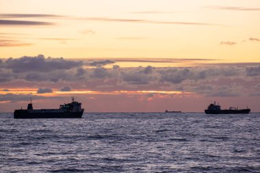 Denizin üzerinde turuncu gün batımı. Endüstriyel gemi yolda. Gökyüzünde güzel bulutlar. Kargo taşımacılığı. Denizci