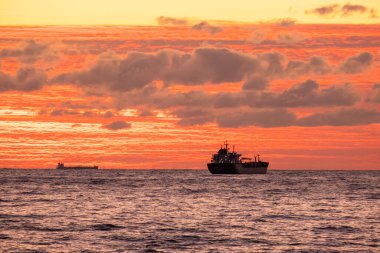 Denizin üzerinde turuncu gün batımı. Endüstriyel gemi yolda. Gökyüzünde güzel bulutlar. Kargo taşımacılığı. Denizci