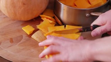 Kız eli, siyah arka planda izole edilmiş tahta tahtada büyük turuncu balkabağı kesiyor. Cadılar Bayramı ve Şükran Günü yemeği konsepti. Kapat.