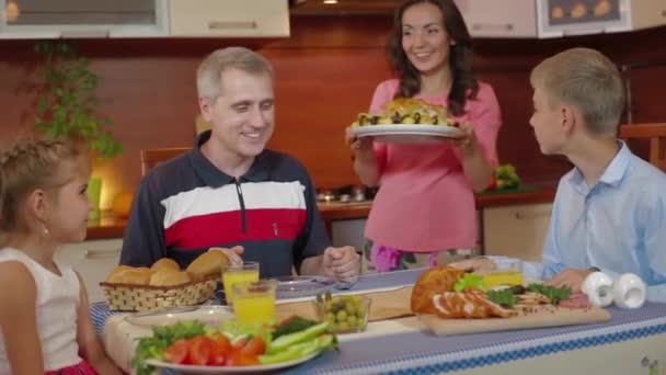 Madre trae plato de pollo horneado del horno en la celebración del cumpleaños de acción de gracias de la familia en la cocina. Amigos saludando, animando. Familia feliz padres, hija e hijo divirtiéndose juntos en la cocina . — Vídeos de Stock