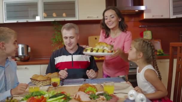 A mãe traz o prato de frango cozido no forno na celebração de aniversário de ação de graças de família na cozinha. amigos cumprimentando, aplaudindo. Feliz família pais, filha e filho se divertindo juntos na cozinha . — Vídeo de Stock