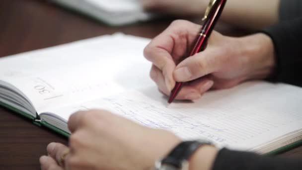 Kvinnlig hand hålla penna och skriva för att göra lista eller affärsdata med penna på bärbara mejeri. Handskrift affärsrapport, anteckna på pappersarbete dokument på kontoret skrivbord i företagets mötesrum. — Stockvideo