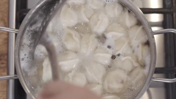 Slow motion top view footage of cooking dumplings in boiling water in pan. Male hand stirs dumplings in saucepan with a colander. Traditional russian food. Food background. — Stock Footage Slow motion top view footage of cooking dumplings in boiling water in pan. Male hand stirs dumplings in saucepan with a colander. Traditional russian food. Food background. Video Clip