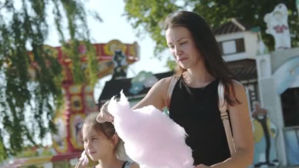 Family walking relaxing in park. Young mother with daughter together walking towards and eating cotton candy in city park. Motherhood and childhood concept. Happy family spending weekend time. — Stock Video