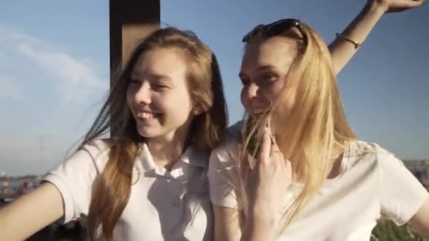 Two young smiling hipster blond women in summer white t-shirt clothes. Girls taking selfie self portrait photos or video on smartphone. Making duck face,show positive grimace — Stock Footage Two young smiling hipster blond women in summer white t-shirt clothes. Girls taking selfie self portrait photos or video on smartphone. Making duck face,show positive grimace Stock Video