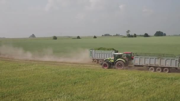 Luftaufnahme Zwei Traktoren fahren auf einer Landstraße aneinander vorbei. Roter Traktor bringt frisch gemähte Futterpflanzen zum Hof über das Feld. Traktor mit leerem Anhänger kehrt zum Verladen von gemähten Pflanzen auf Feld zurück — Stockvideo