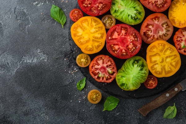 Tomates coloridos orgánicos frescos en plato negro, fondo oscuro —  Fotos de Stock