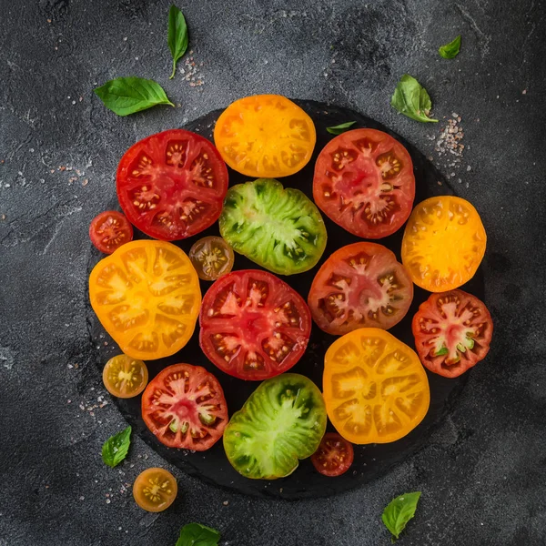 Tomates coloridos orgánicos frescos en plato negro, fondo oscuro —  Fotos de Stock