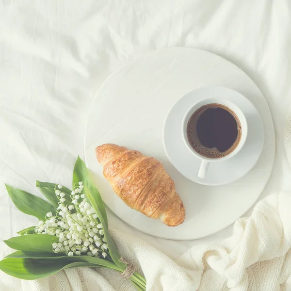 Breakfast in bed. croissant, cup of coffee and  Lily of the vall — Stock Photo, Image