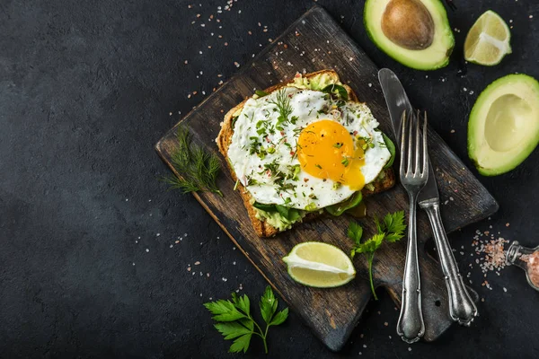 Toast with avocado, spinach and fried egg on wooden cutting boar — Stock Photo, Image