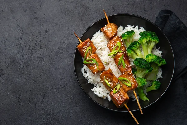 Teriyaki salmon skewers with rice and broccoli on black plate — Stock Photo, Image