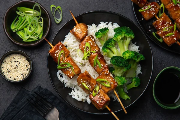 Teriyaki salmon skewers with rice and broccoli on black plate — Stock Photo, Image