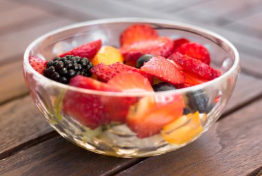 Ahşap masa üzerinde bir cam kasede servis renkli meyve salatası yakın çekim.