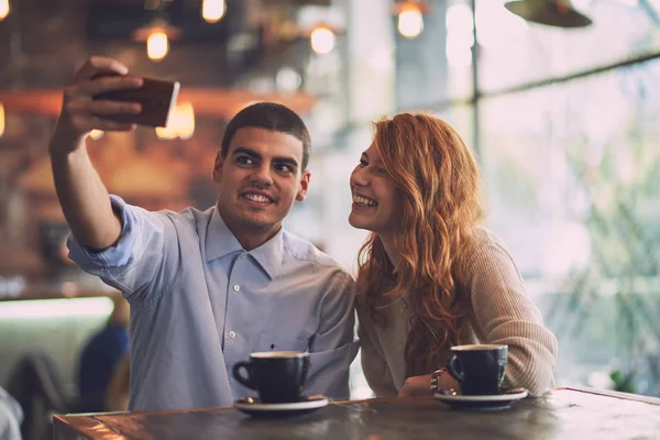 Mężczyzna z kobietą czyniąc selfie w kawiarni — Zdjęcie stockowe