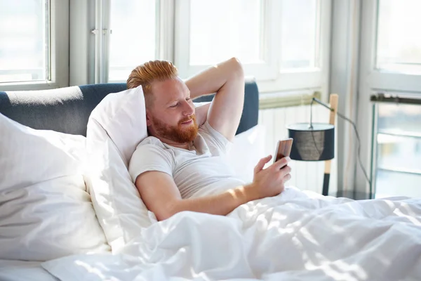 Man with phone in bed — Stock Photo, Image