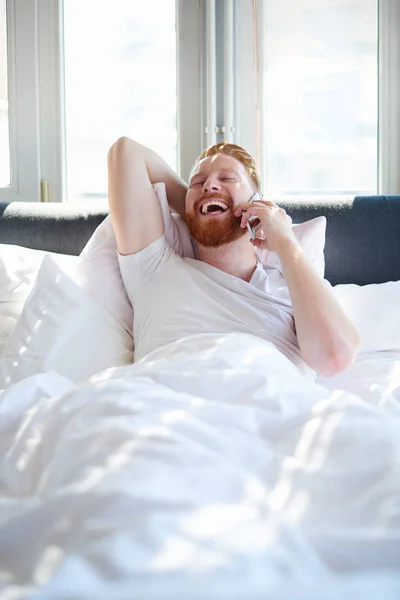 Человек с телефоном в постели — стоковое фото