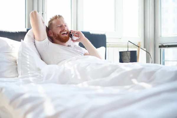 ベッドで電話を持つ男 — ストック写真