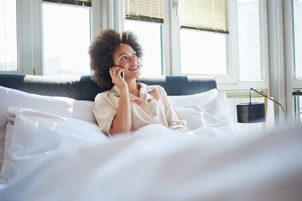 Kvinne som snakker i mobiltelefon i sengen – stockfoto