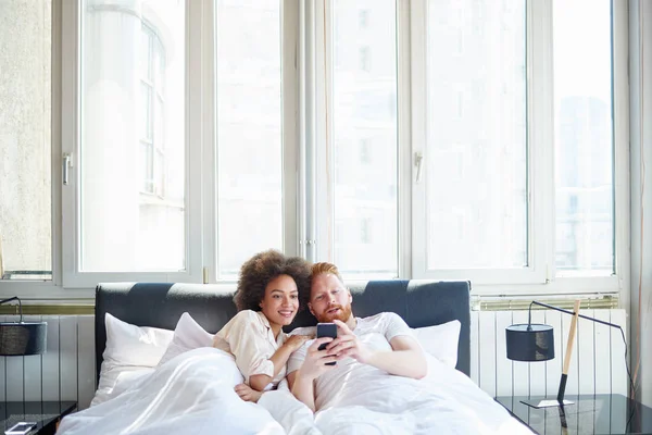 Couple watching video on phone in bed — Stock Photo, Image