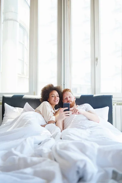 Paar kijken naar video op telefoon in bed — Stockfoto