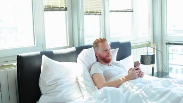 Man met telefoon in bed — Stockvideo