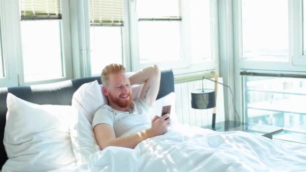 Man met telefoon in bed — Stockvideo