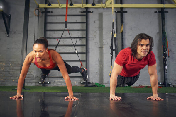 Young mixed race female and male athletes training in gym with sport equipment