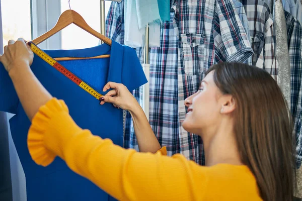 Gülümseyen beyaz tenli moda tasarımcısı stüdyosunda dikilirken elbisesini ölçüyor.. — Stok fotoğraf