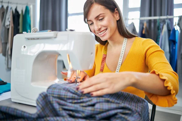 Attraente sarta caucasica laboriosa seduta nel suo studio e cucire vestiti . — Foto Stock