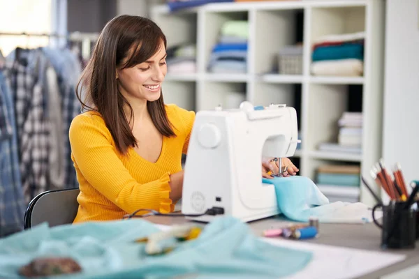 Smiling charming caucasian fashion designer sitting in her studio and sewing beautiful evening dress. — Stockfoto