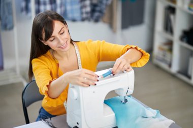 Kendini işine adamış bir terzi atölyesinde oturup dikiş makinesine iplik sokuyor..