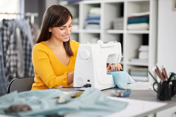 Sonriendo encantadora diseñadora de moda caucásica sentada en su estudio y cosiendo hermoso vestido de noche . —  Fotos de Stock