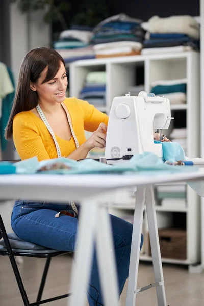 Smiling charming caucasian fashion designer sitting in her studio and sewing beautiful evening dress. — Stock Photo, Image