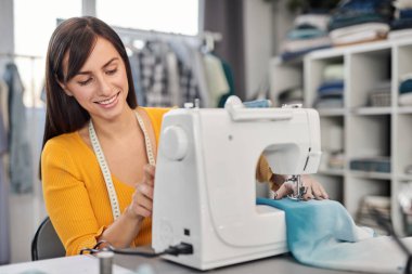 Gülümseyen beyaz tenli moda tasarımcısı stüdyosunda oturuyor ve güzel bir gece elbisesi dikiyor..