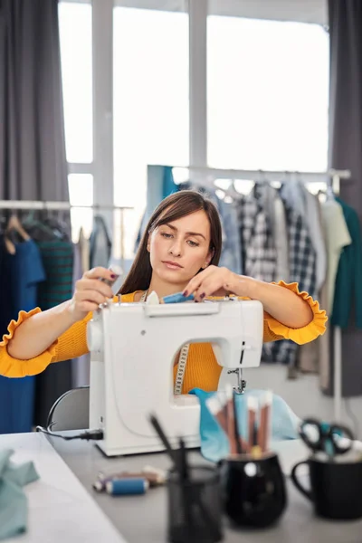 Cucitrice dedicata seduta nel suo studio e che inserisce il filo nella macchina da cucire . — Foto Stock