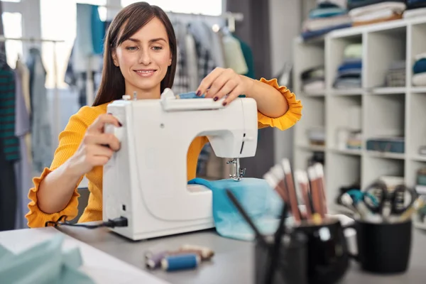 Toegewijde naaister zittend in haar studio en inbrengende draad in naaimachine. — Stockfoto